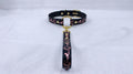 A black collar with a gold-colored buckle and a pink floral pattern on the strap is displayed against a white background.