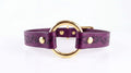 A purple leather collar with a gold-colored circular buckle and floral designs on the straps.
