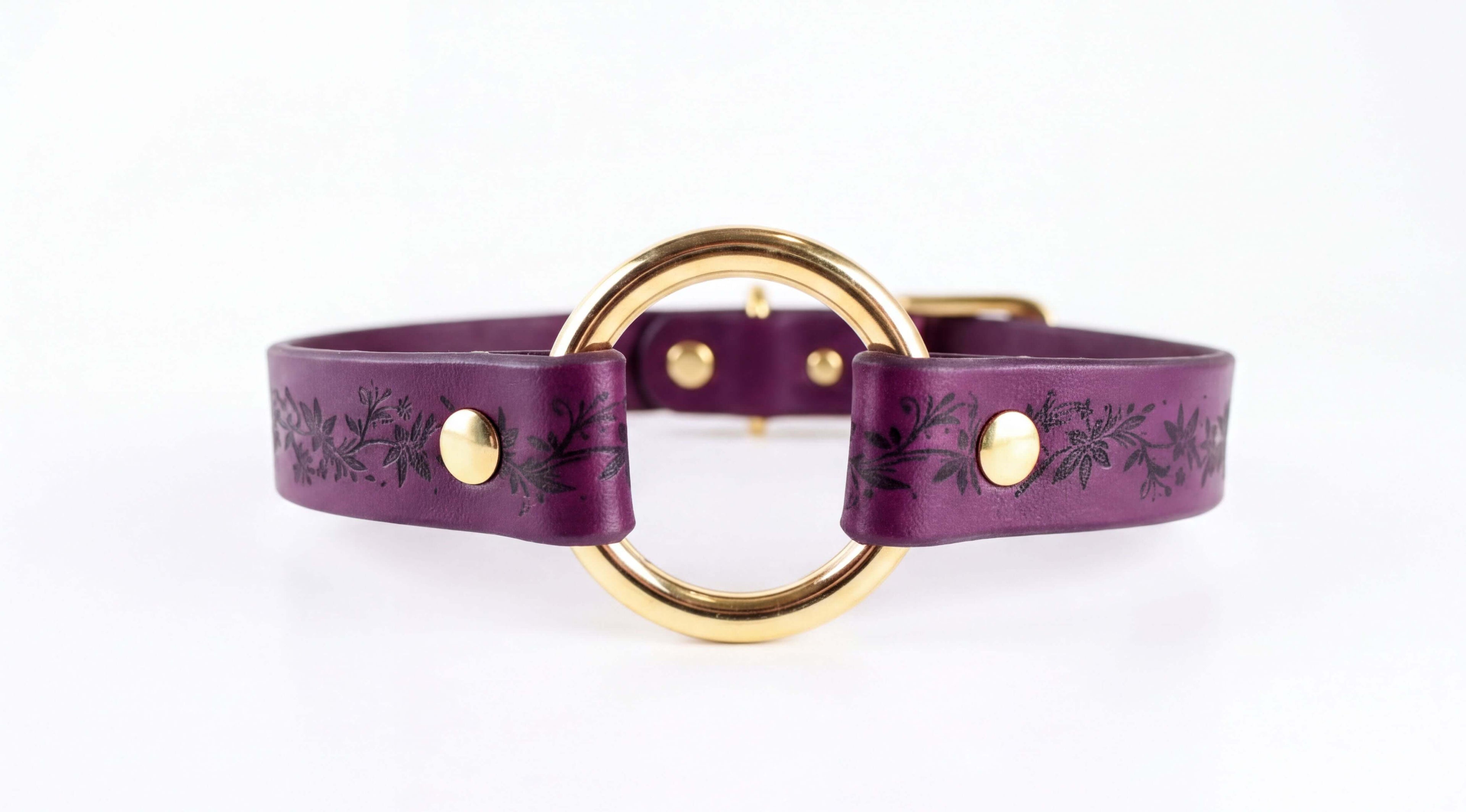 A purple leather collar with a gold-colored circular buckle and floral designs on the straps.