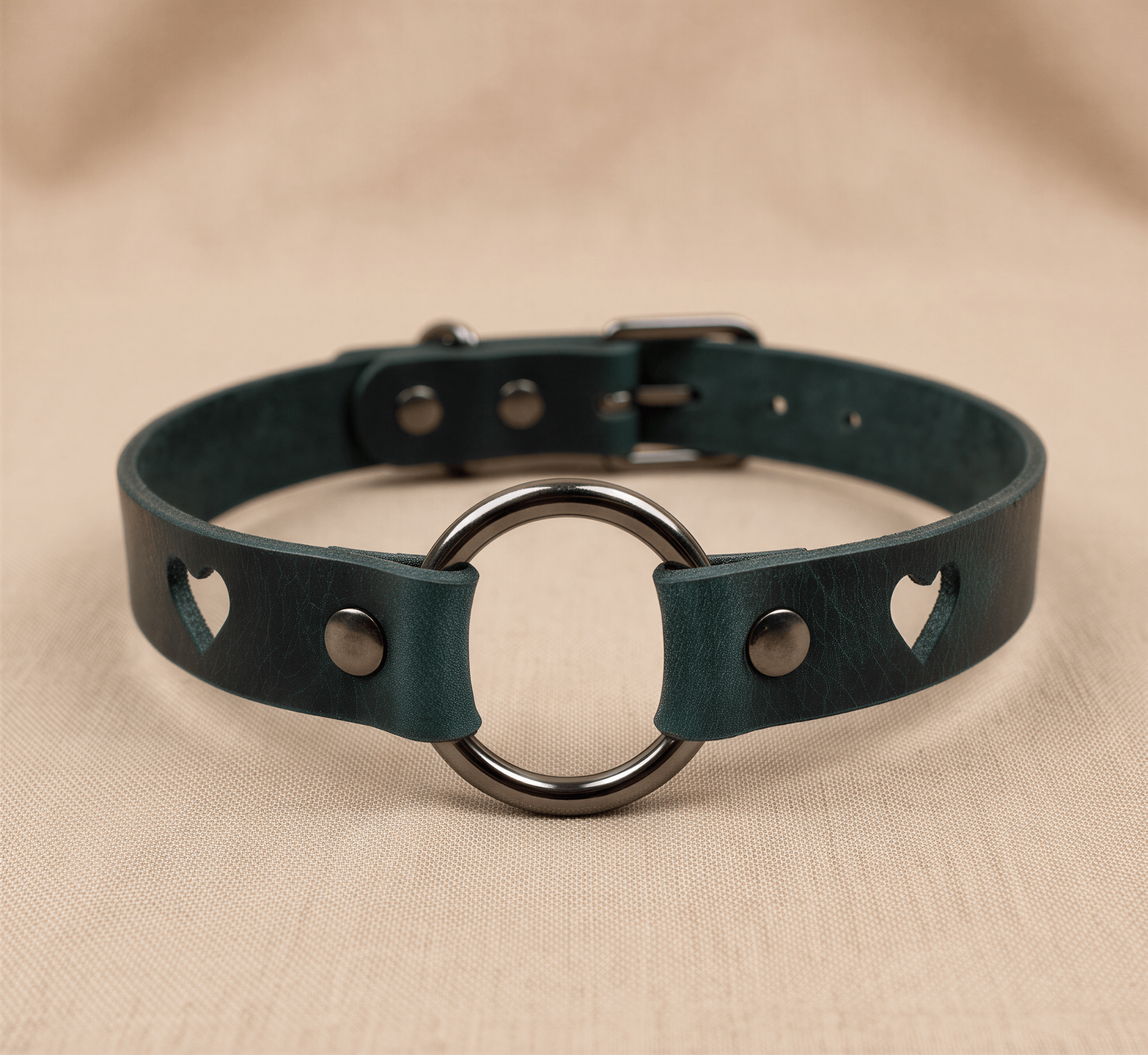 A dark green leather choker necklace with a metal ring and heart-shaped cutouts on the sides.
