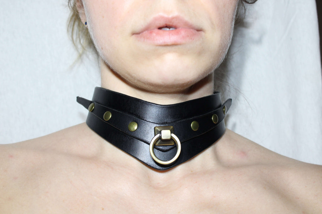 A close-up of a person's neck wearing a black leather choker with a metal ring and studs.