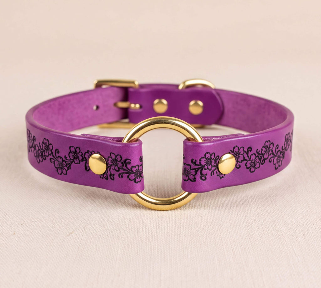 A purple leather collar with a gold-colored metal ring and decorative floral patterns.