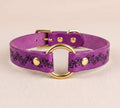A purple leather collar with a gold-colored metal ring and decorative floral patterns.