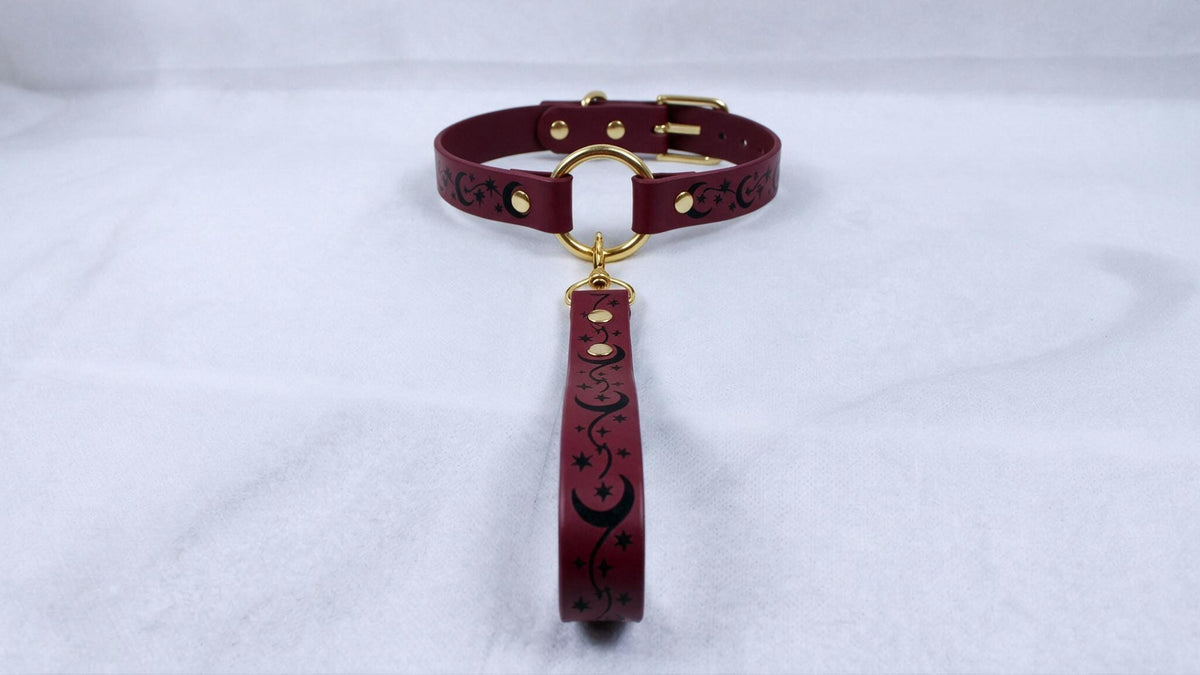 A burgundy leather collar with a gold buckle and a black star-and-crescent design on the strap.