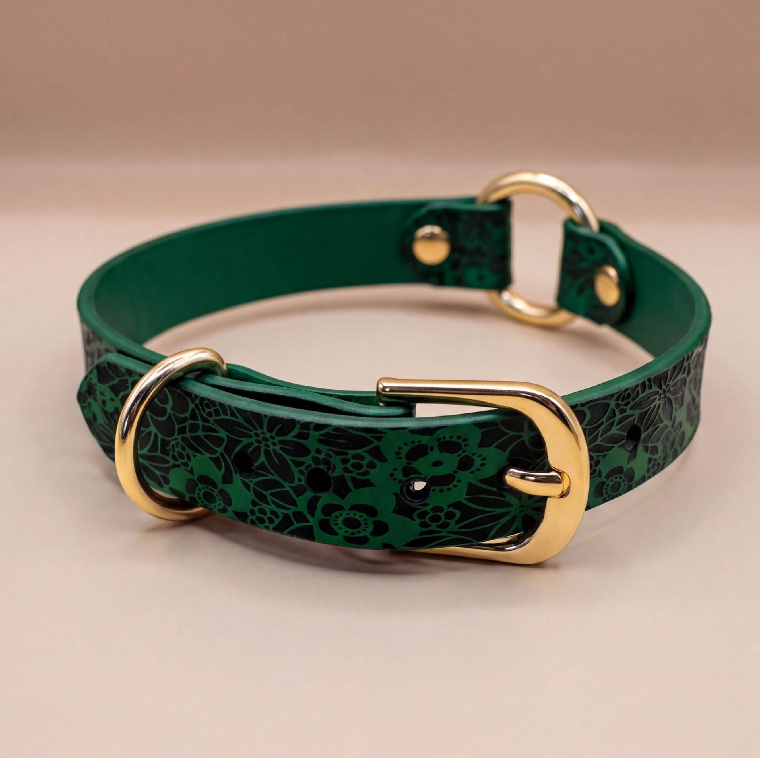 A green leather collar with a floral pattern and two gold buckles.