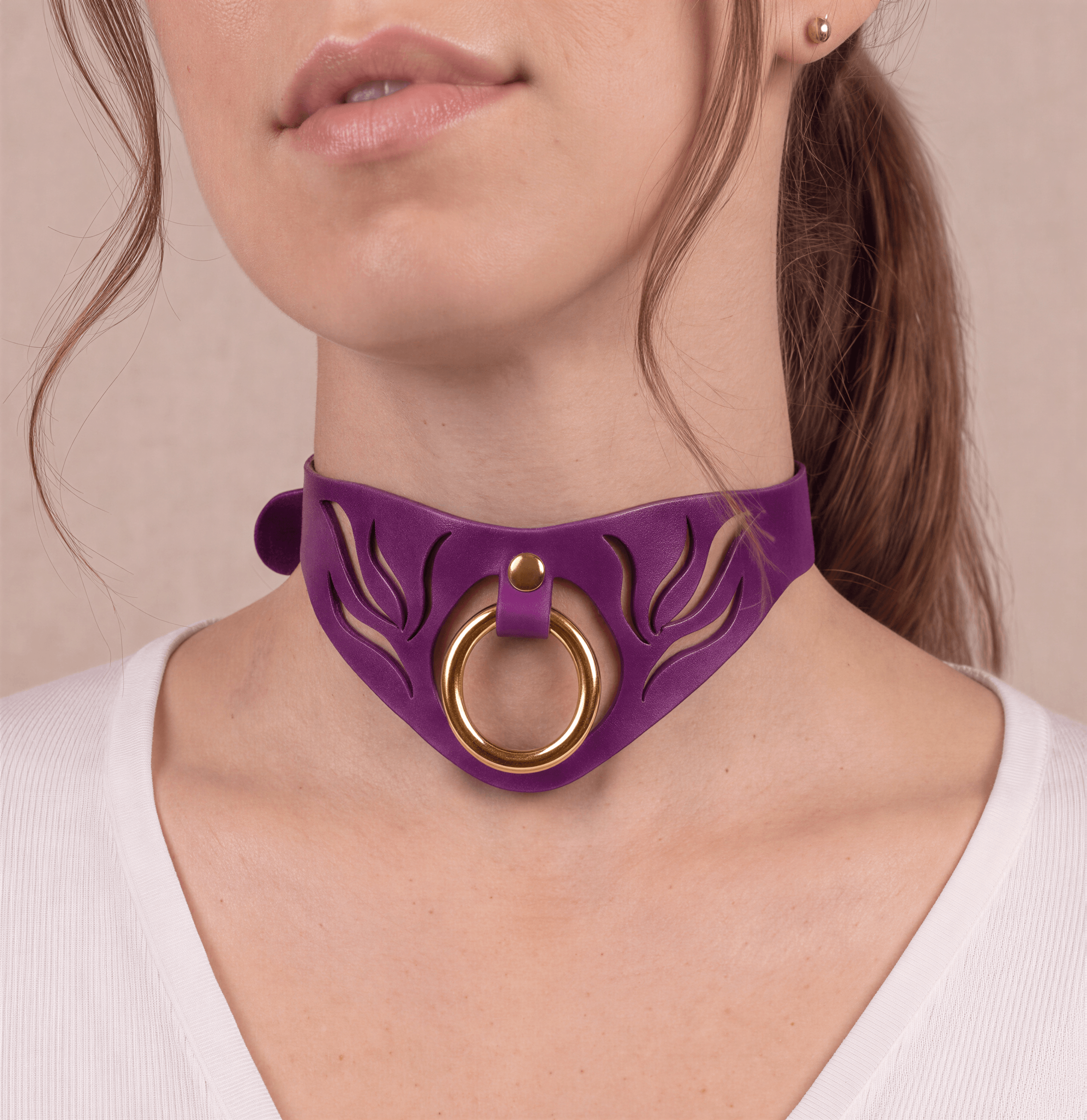 A close-up of a woman's neck and chest area, featuring a purple choker necklace with a gold ring and a floral design.