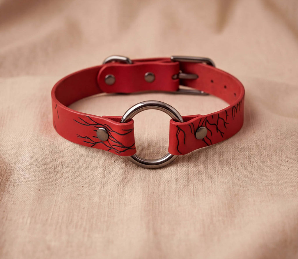 A red leather collar with a metal ring and a black design on the surface.