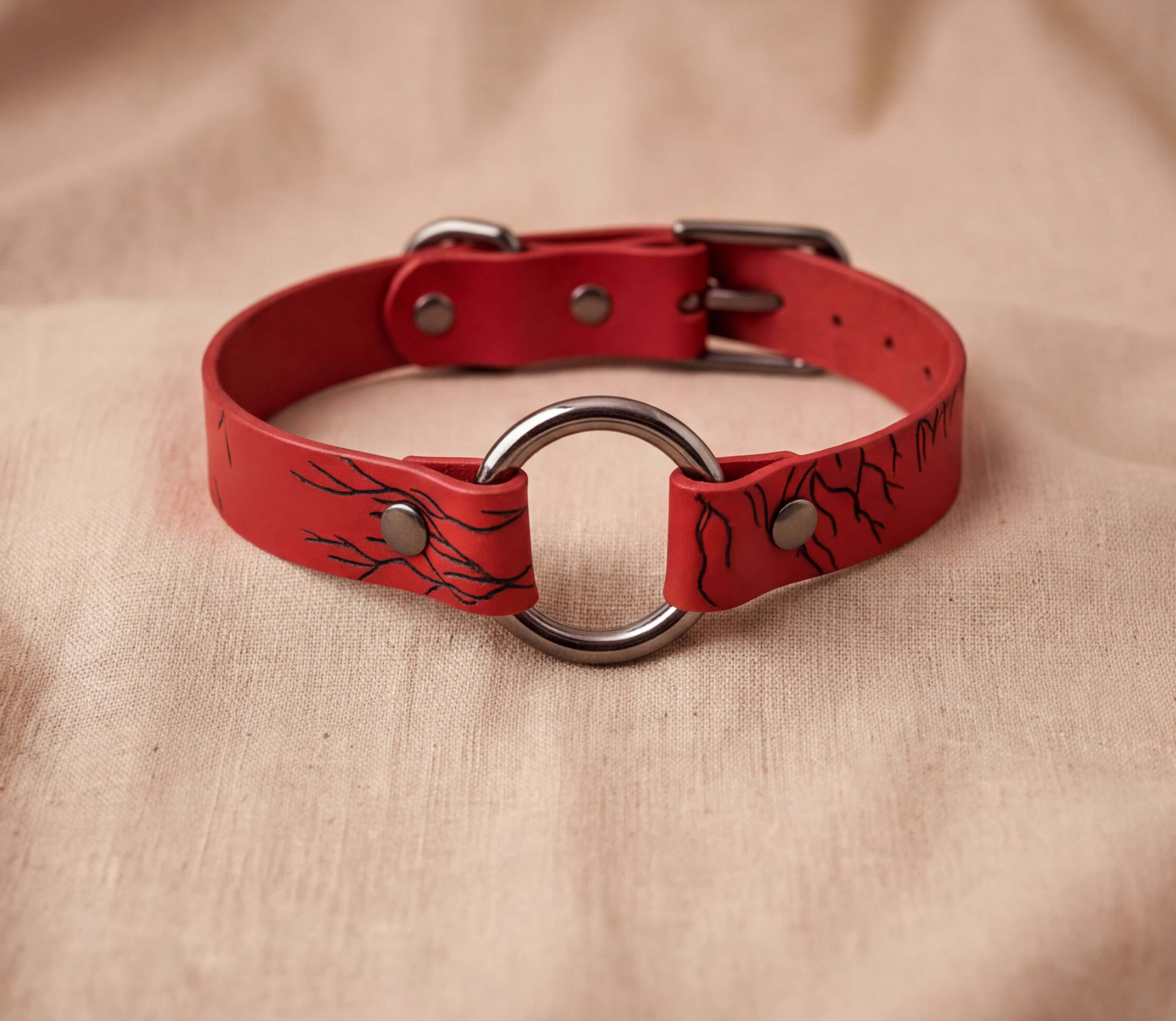 A red leather collar with a metal ring and a black design on the surface.