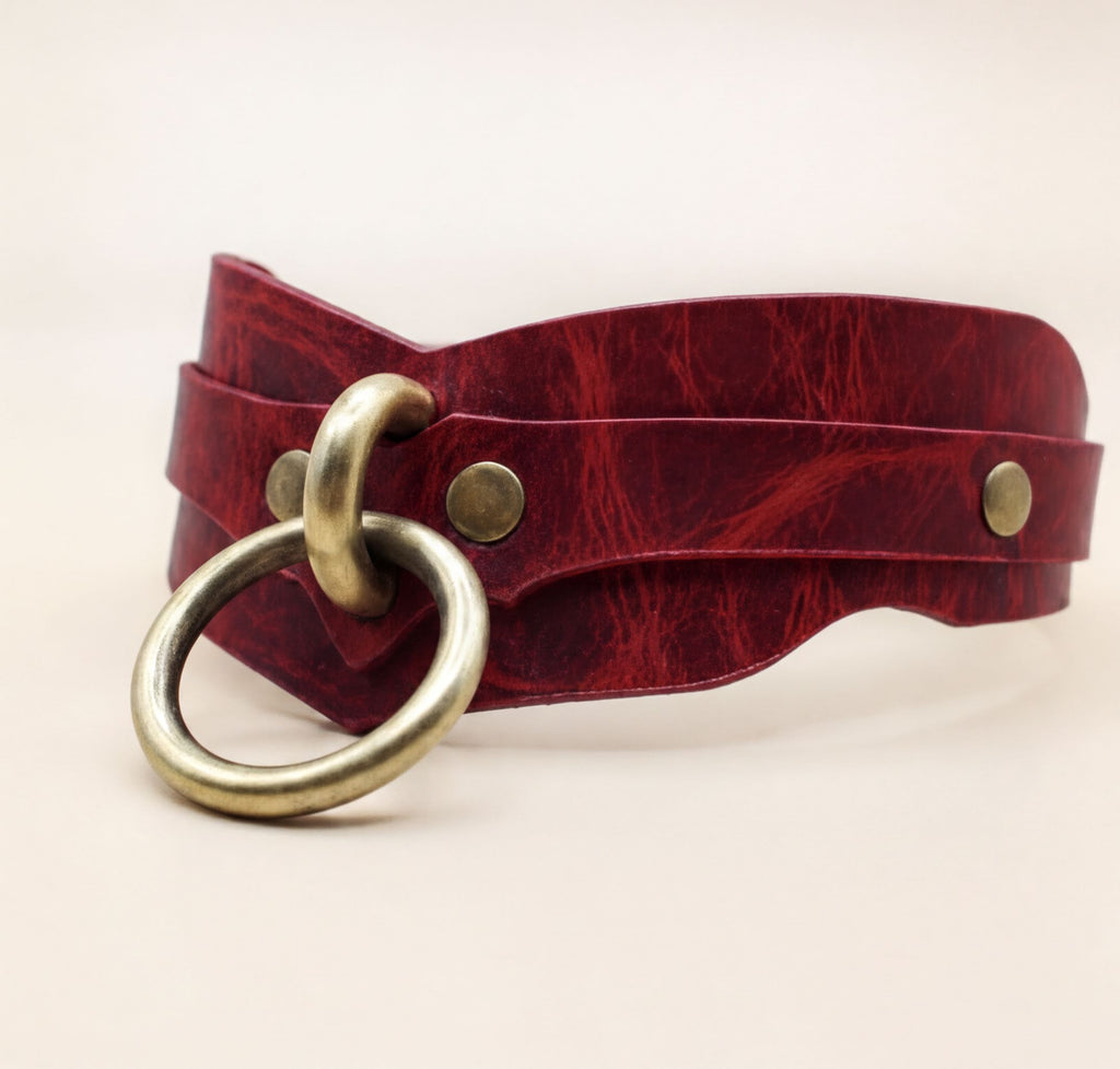 A red leather choker necklace with a brass ring and two brass buttons.