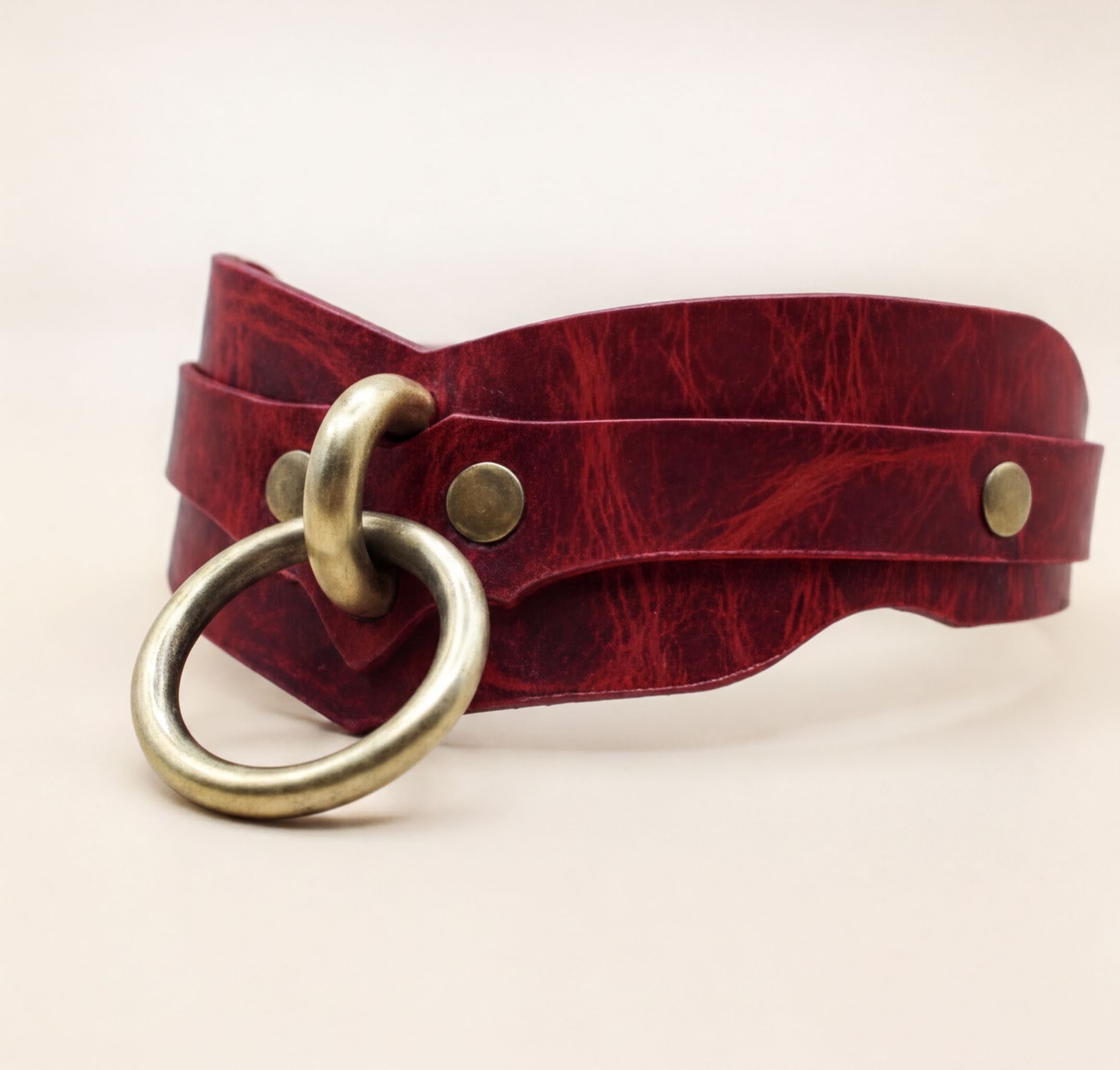 A red leather choker necklace with a brass ring and two brass buttons.