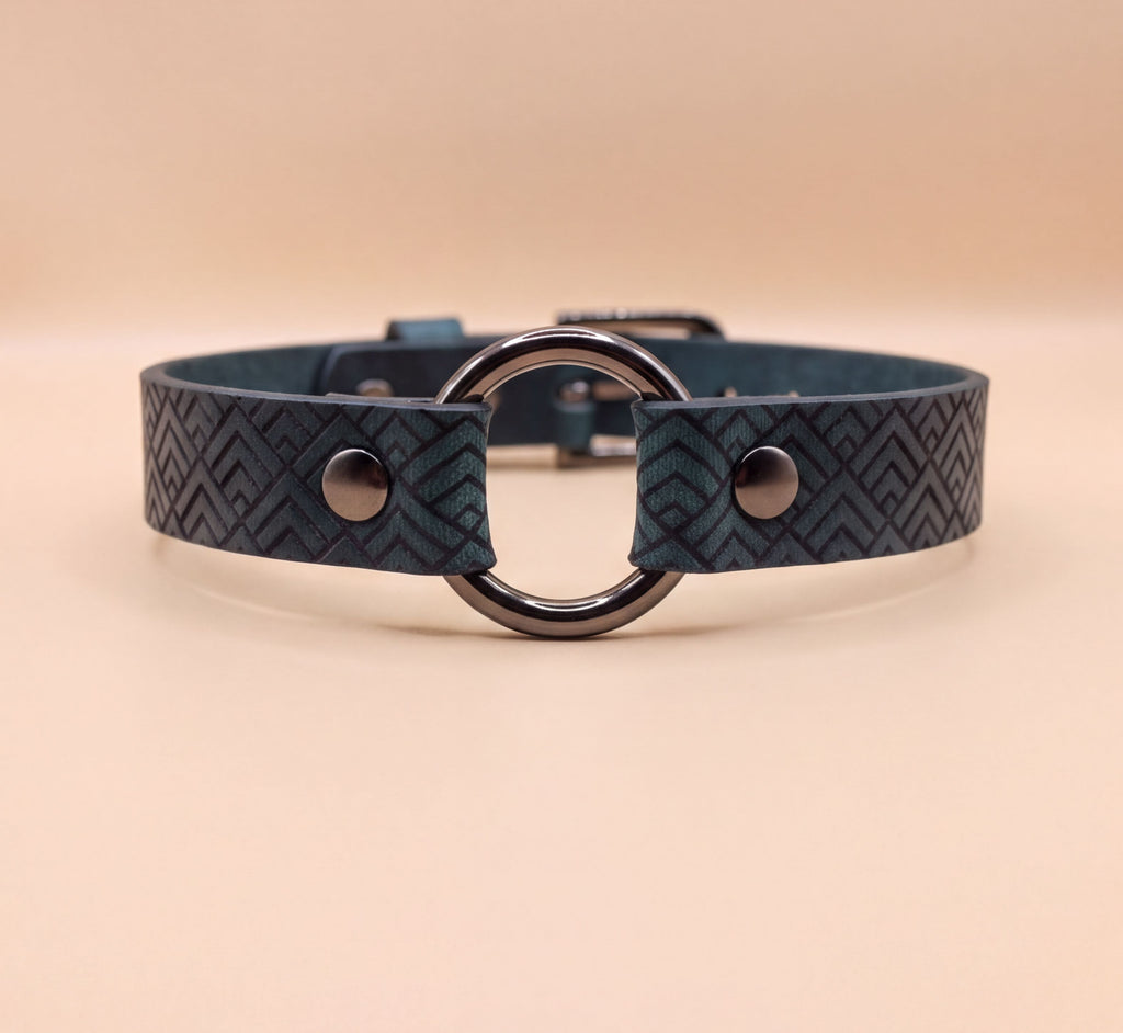 A close-up view of a dark blue leather choker collar with a metal ring and two metal buttons.