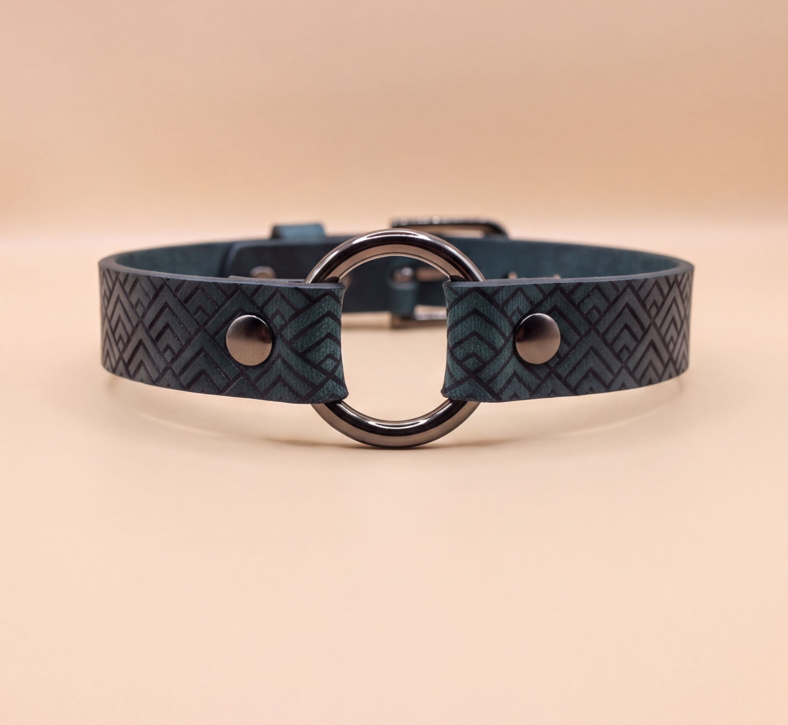 A close-up view of a dark blue leather choker collar with a metal ring and two metal buttons.