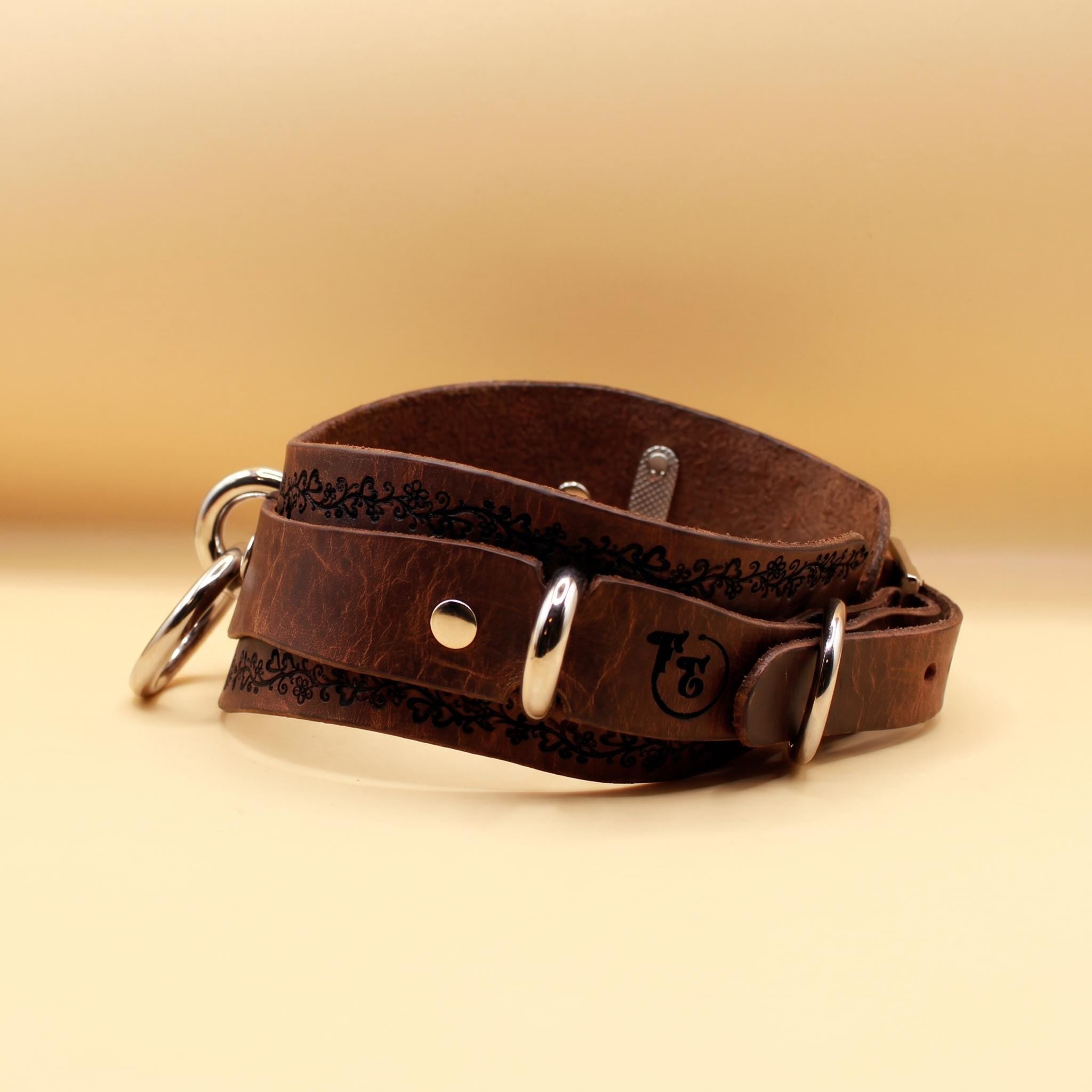 A brown leather dog collar with metal rings and a logo on it, placed on a yellow background.