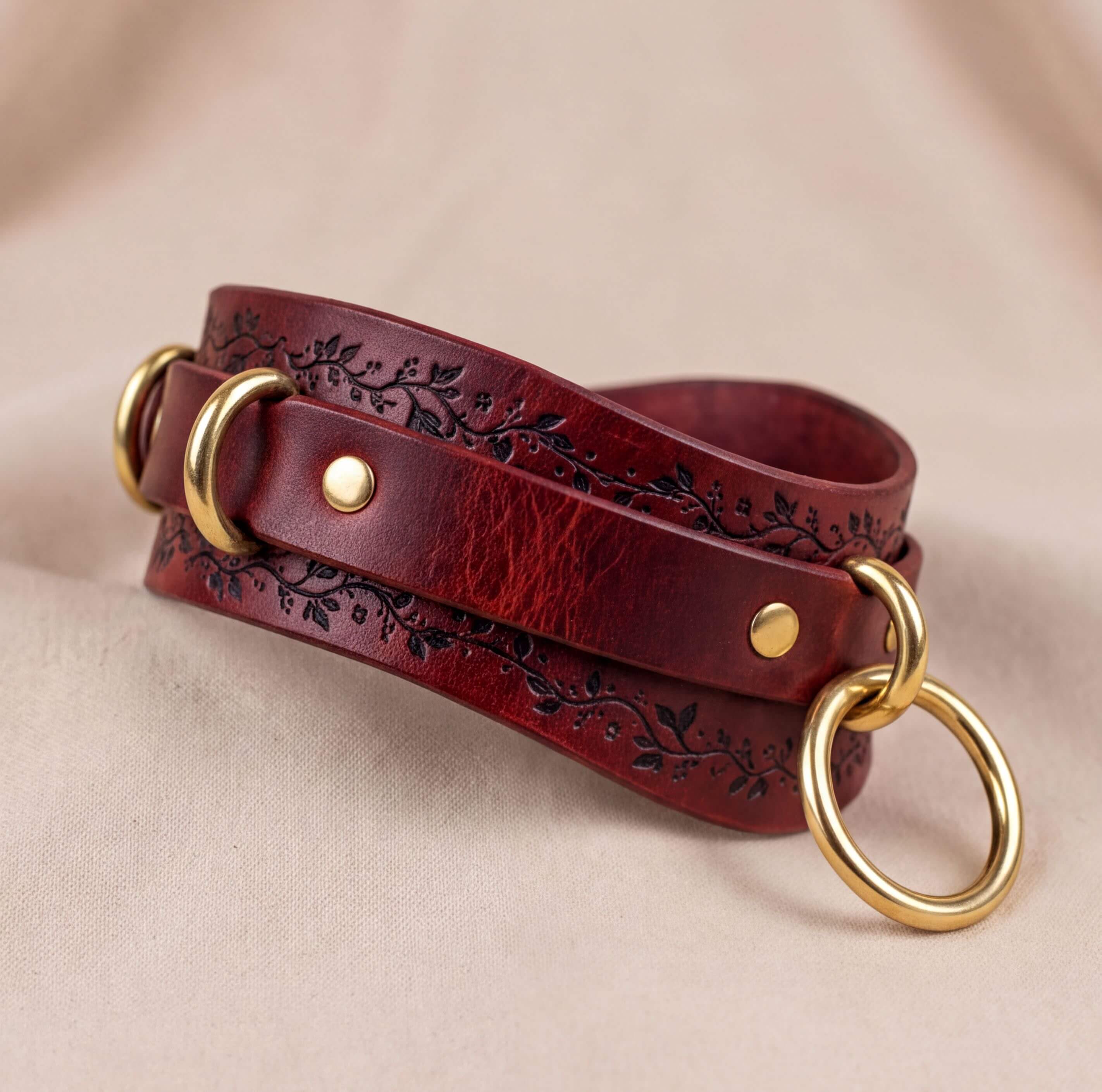 A burgundy leather strap with gold rings and a floral design on the edges, resting on a beige background.