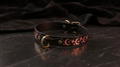 A black leather collar with a metallic buckle and a starry night sky design on it, resting on a dark surface.