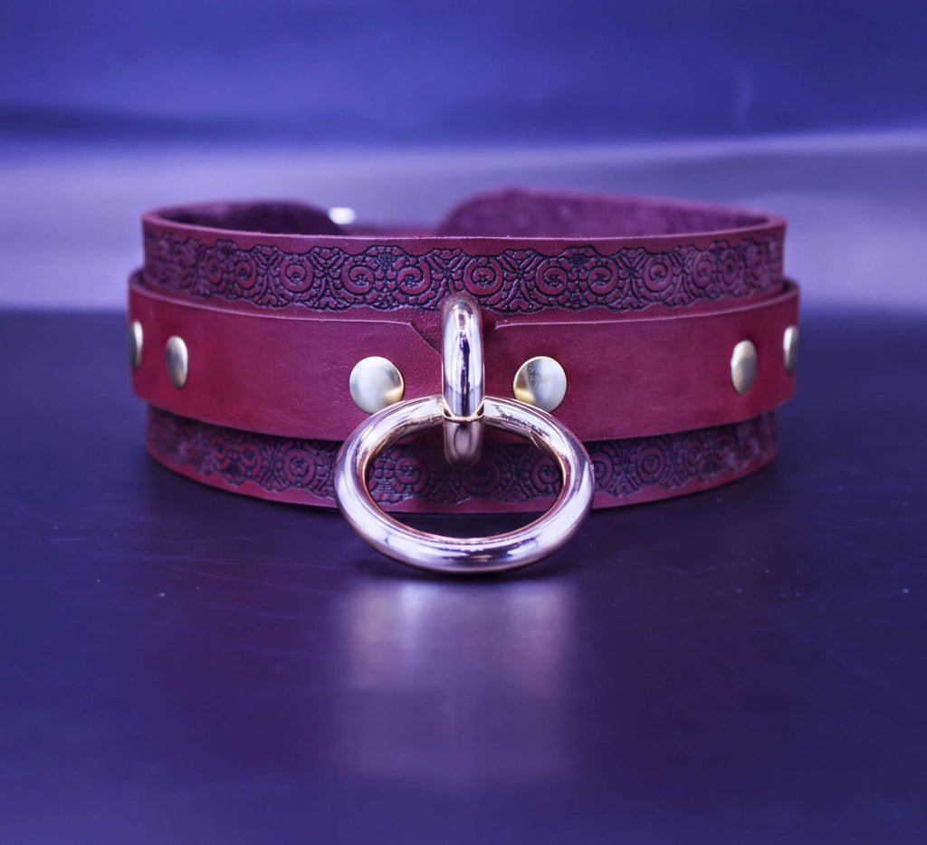 A burgundy leather choker necklace with a metal ring and decorative elements on the band.