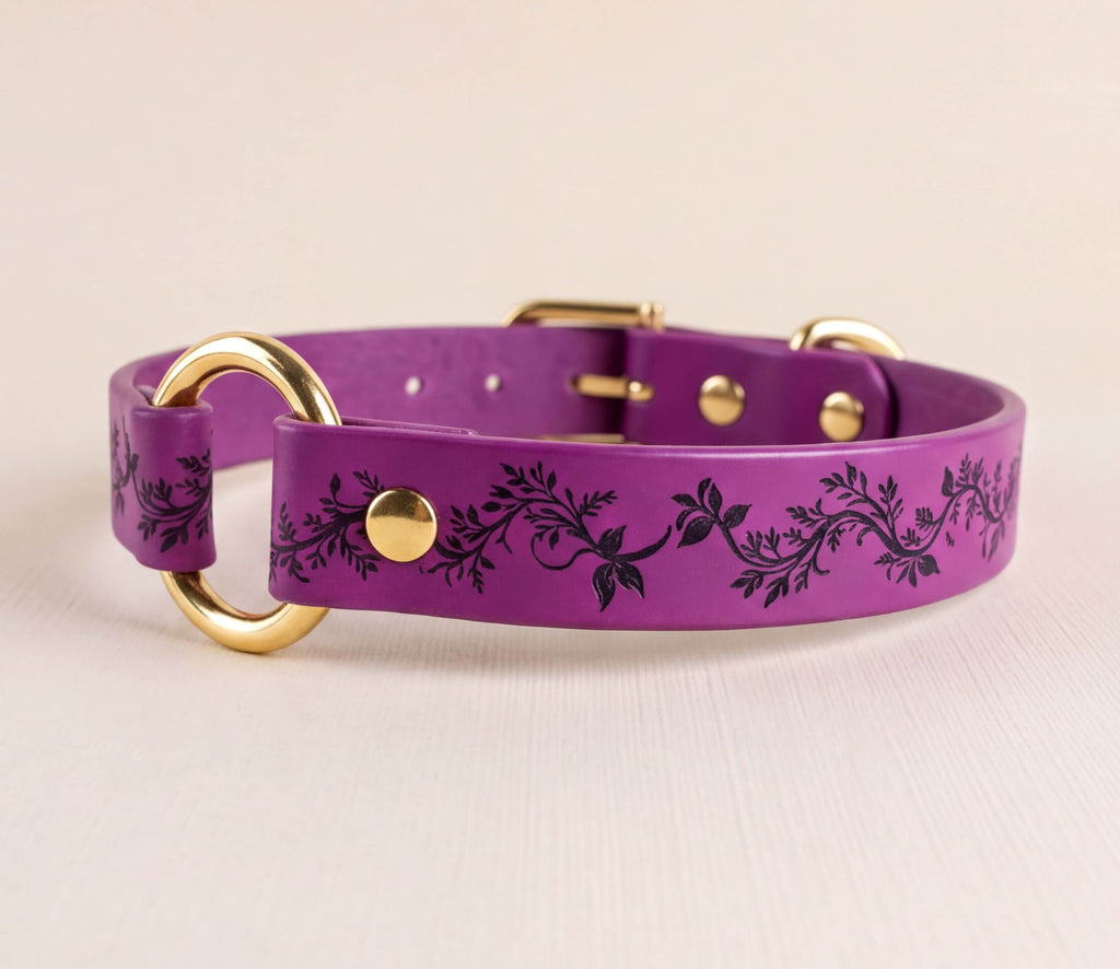 A purple leather dog collar with a floral pattern and gold-colored metal rings.
