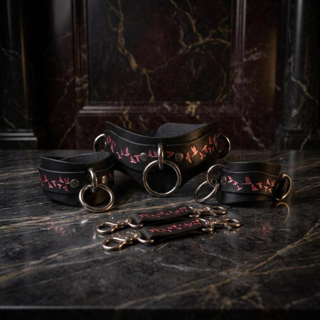 a set of black leather choker necklaces with pink bird designs, arranged on a marble surface.