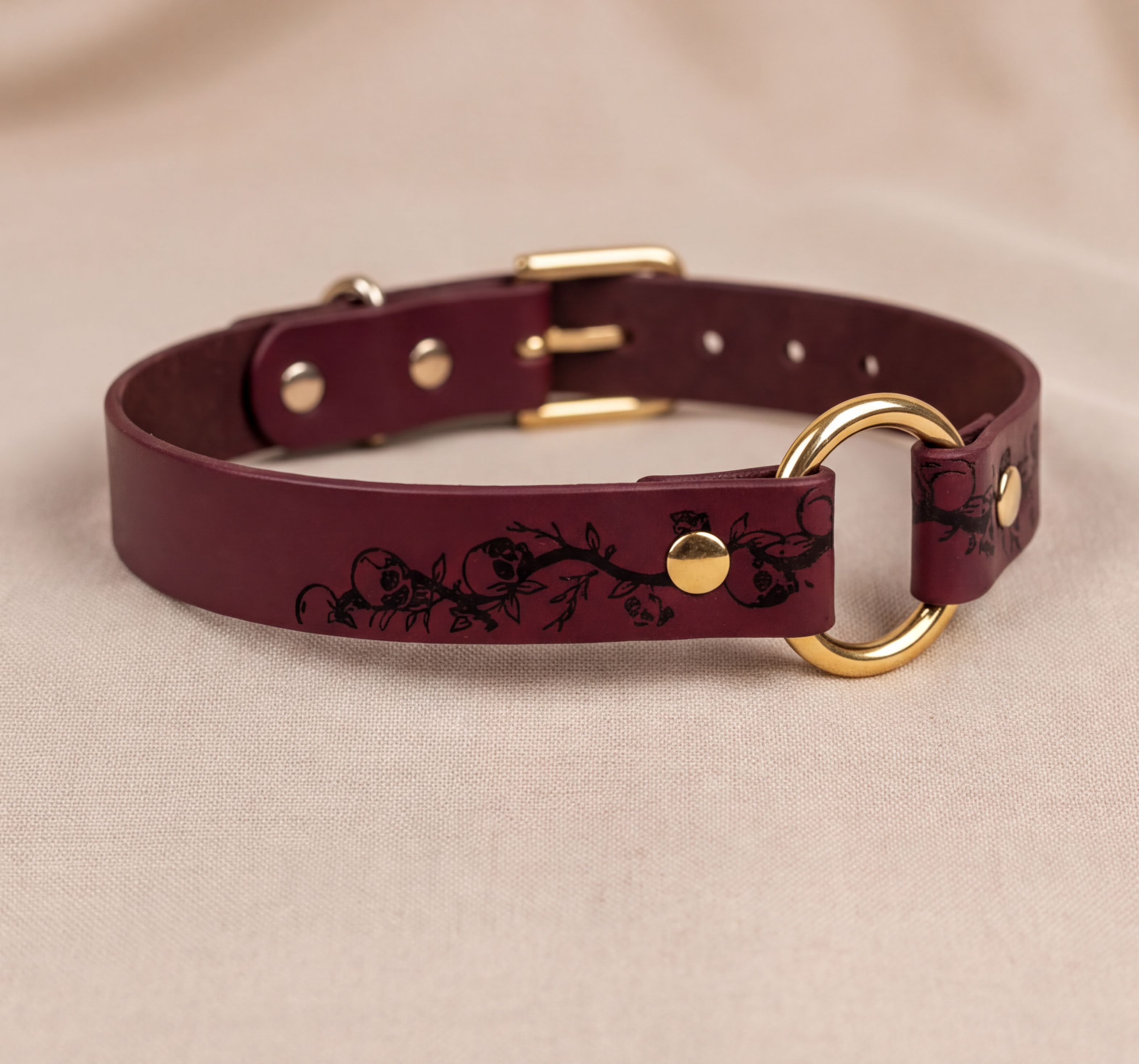 A burgundy leather collar with a gold-colored buckle and a floral design on the strap.