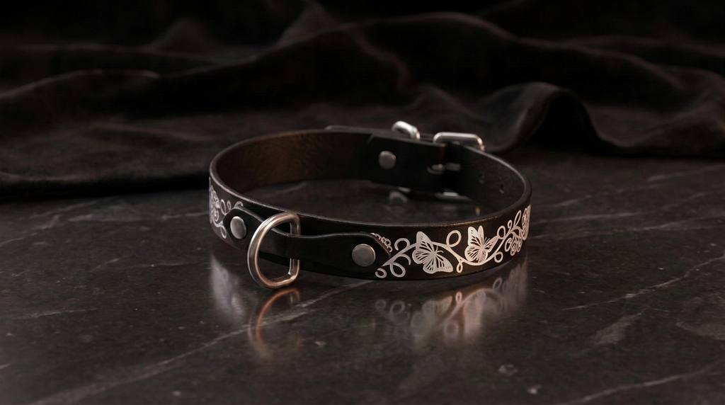 A black leather collar with a silver metal buckle and floral design on a dark background.