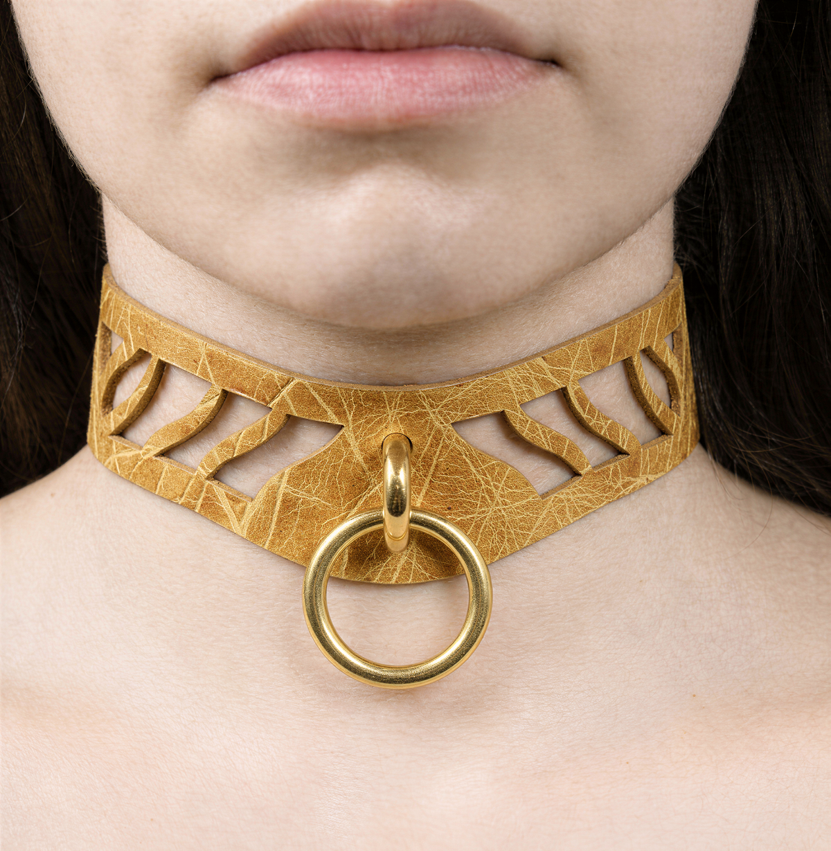 A close-up of a woman's neck and chest area wearing a gold-colored choker necklace with a circular ring.