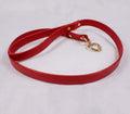 A red leather leash with a heart-shaped metal attachment is shown on a white surface.