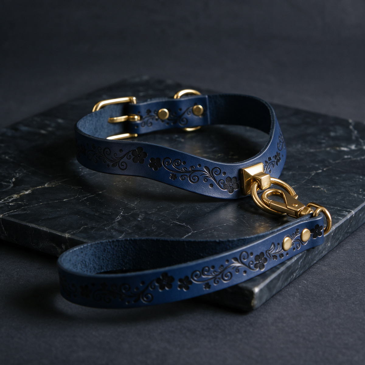 A blue leather dog collar with a gold-colored buckle and a matching leash is displayed on a dark surface.
