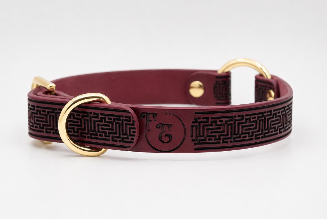 A burgundy leather dog collar with a black maze pattern and two gold-colored buckles.