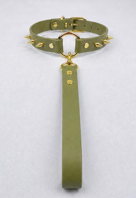 A green leather collar with spikes and a gold-colored metal ring attached to it.