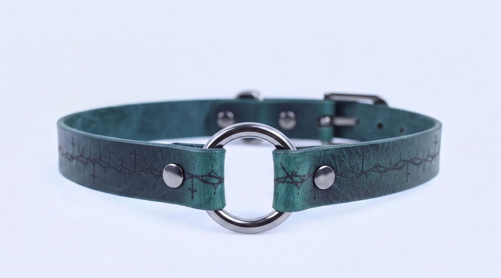 A close-up image of a green leather collar with a metal ring and buckle.