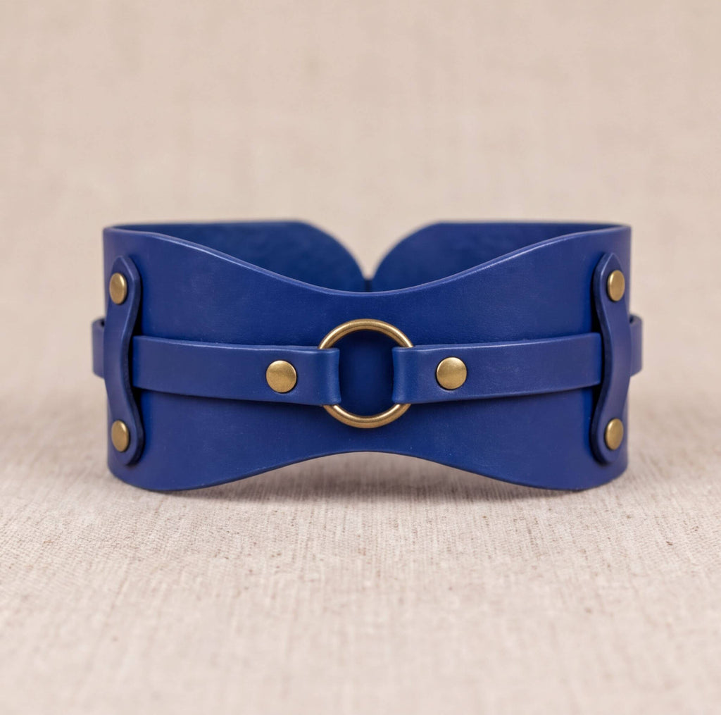 A blue leather corset with a gold ring buckle, displayed on a beige background.