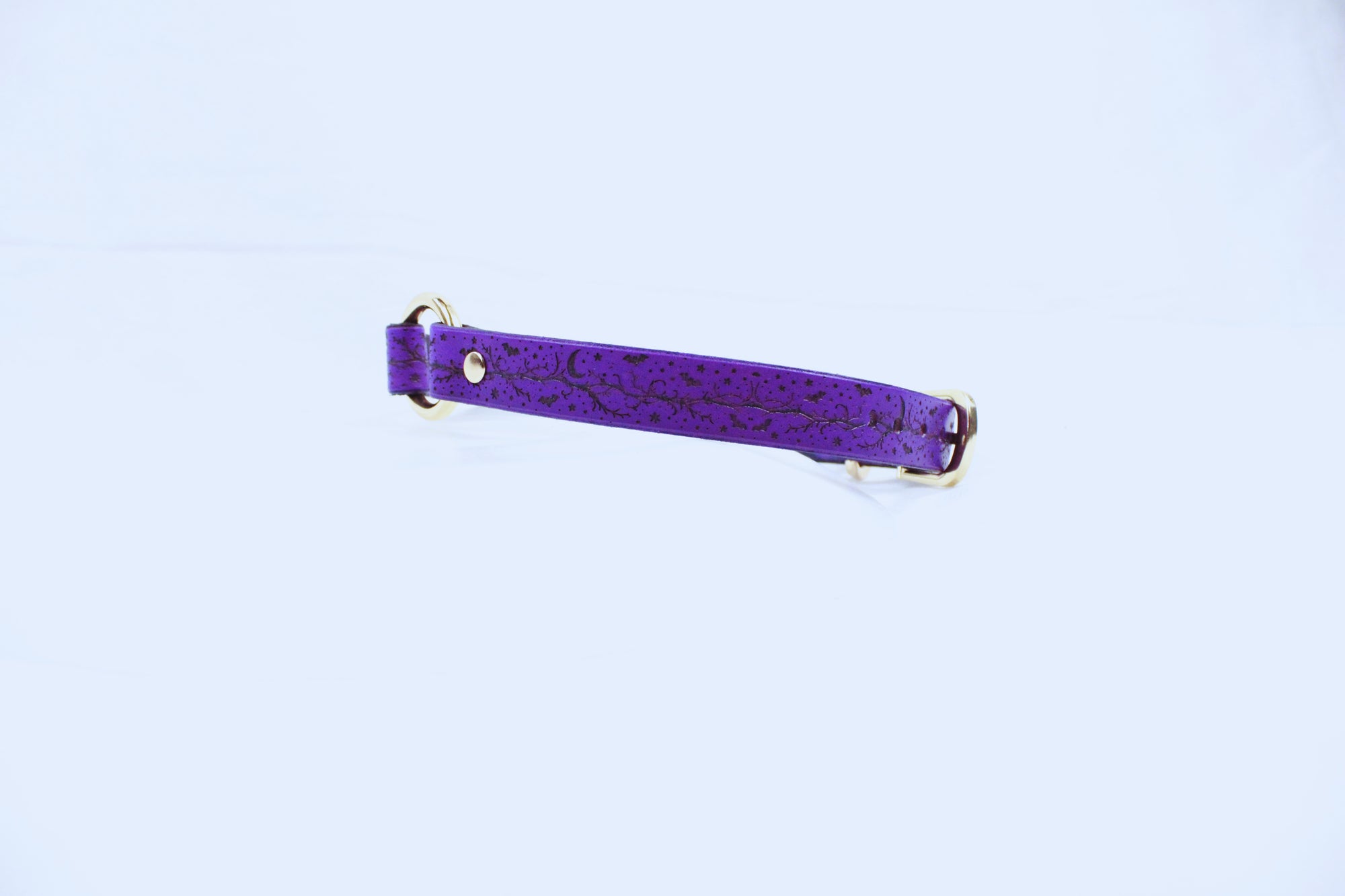 A purple leather strap with a floral pattern, featuring two gold buckles, is shown against a white background.