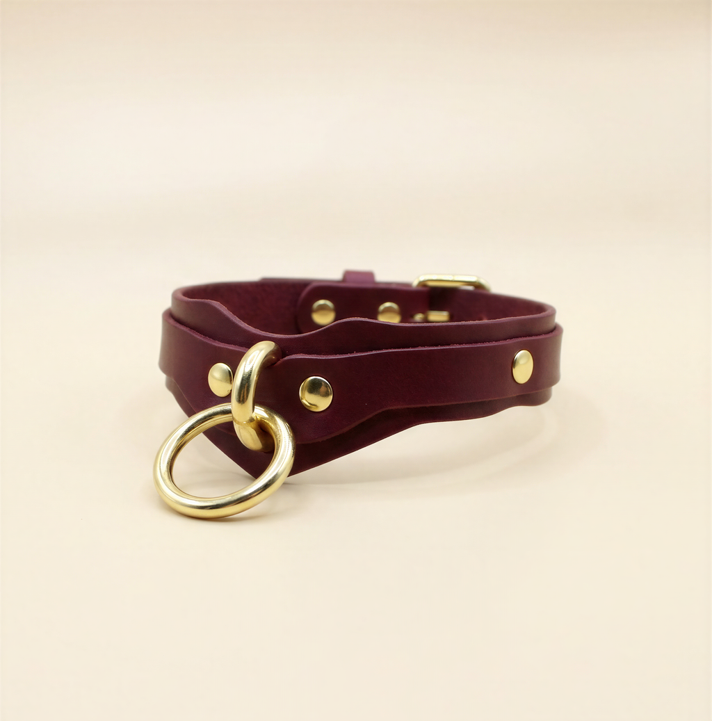 A burgundy leather choker necklace with a gold-colored metal ring and a gold-colored metal buckle.