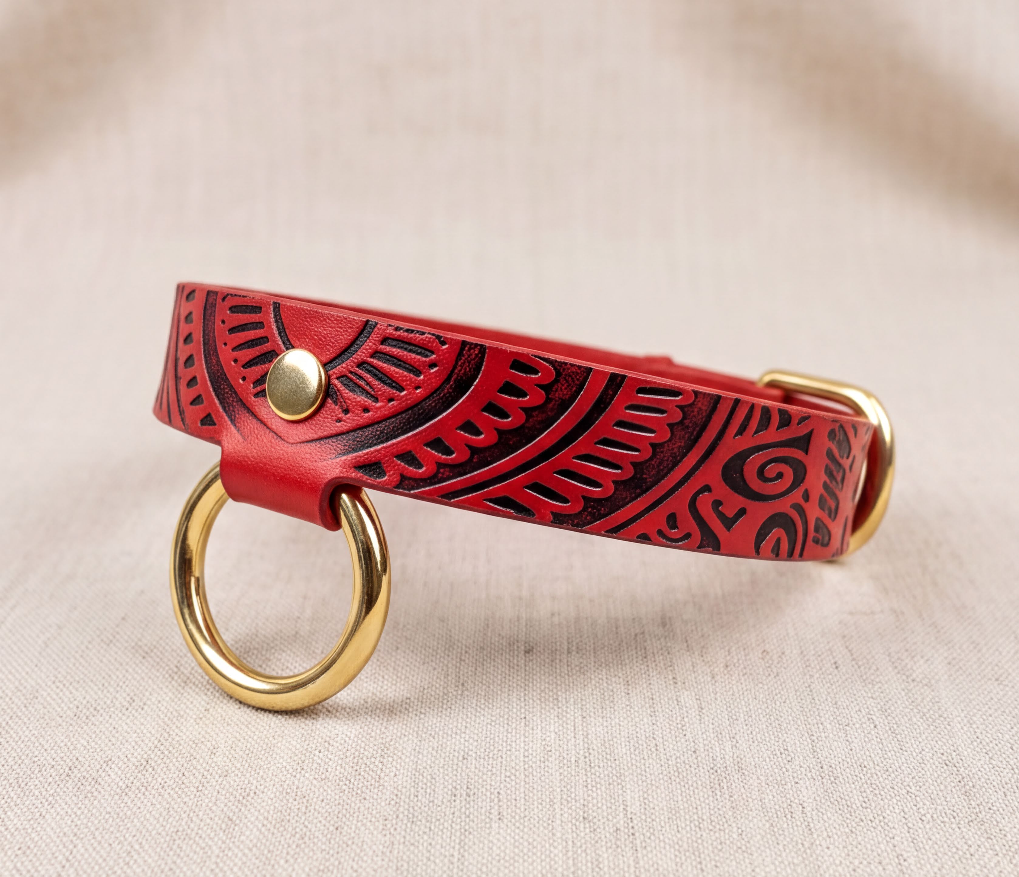 A red leather collar with a gold ring and a decorative pattern on it.