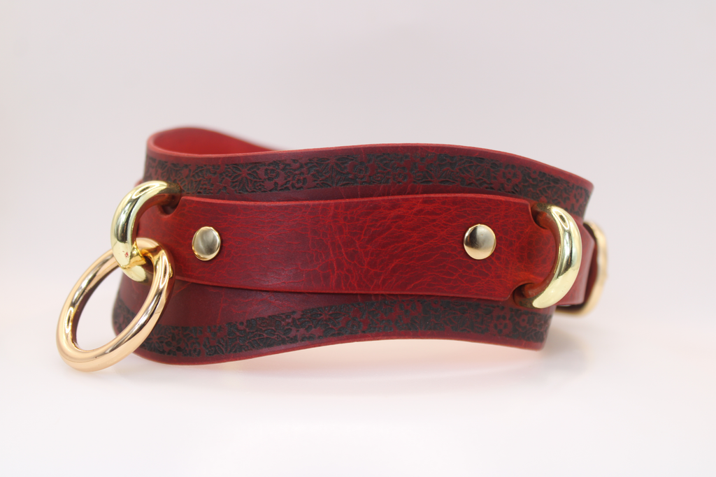 A red leather choker necklace with gold-colored metal rings and a decorative pattern on the leather.