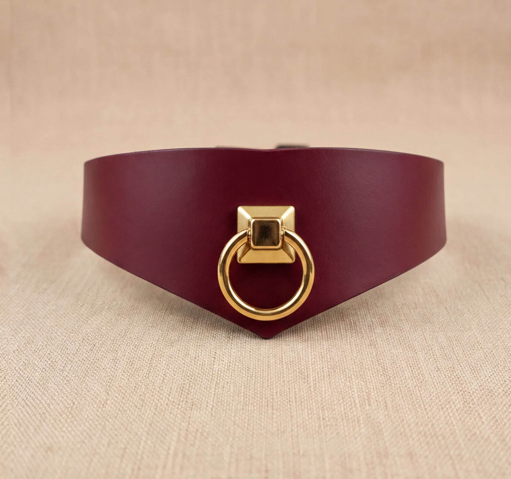 A burgundy leather choker necklace with a gold-colored metal ring on the front.