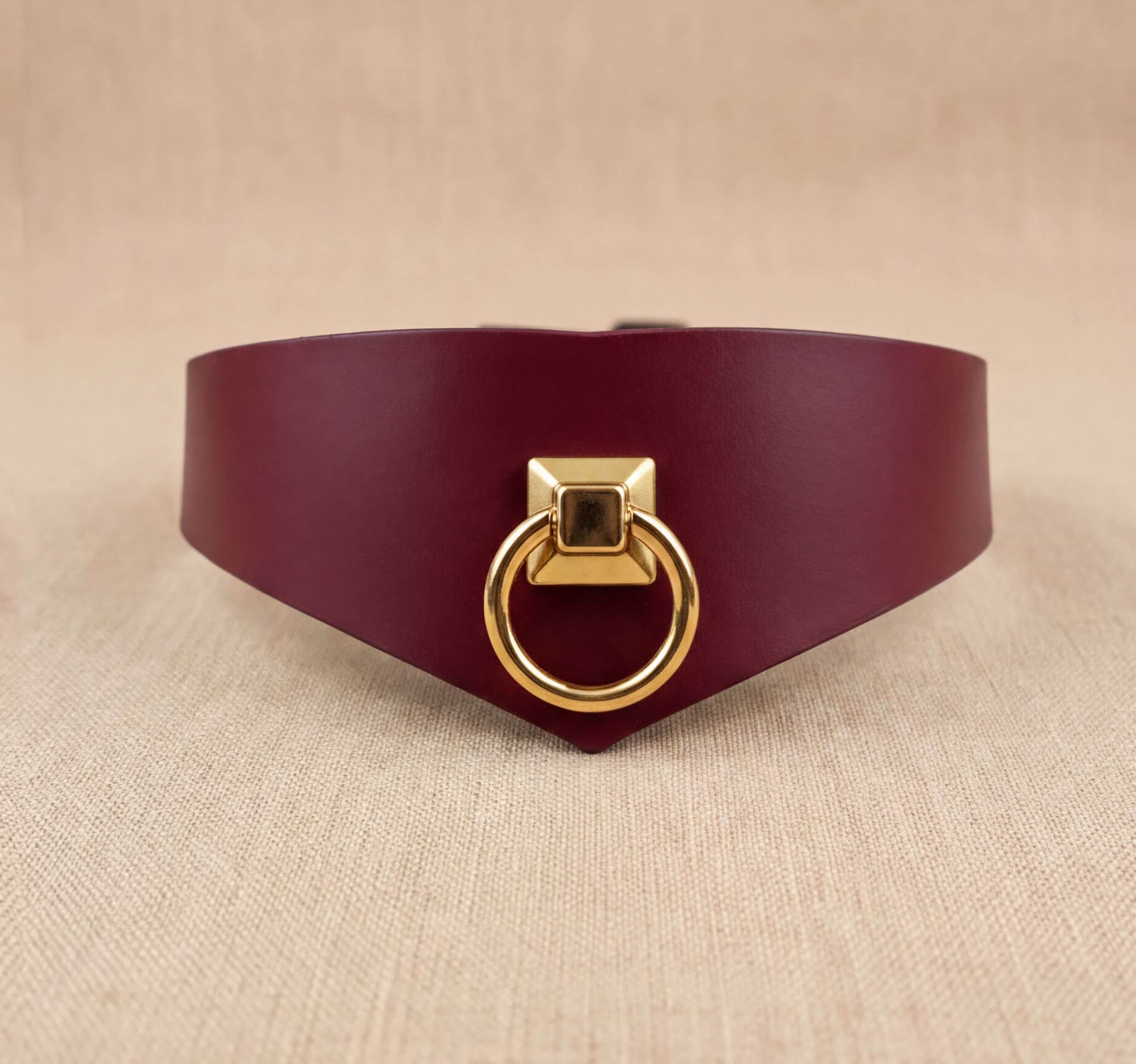 A burgundy leather choker necklace with a gold-colored metal ring on the front.