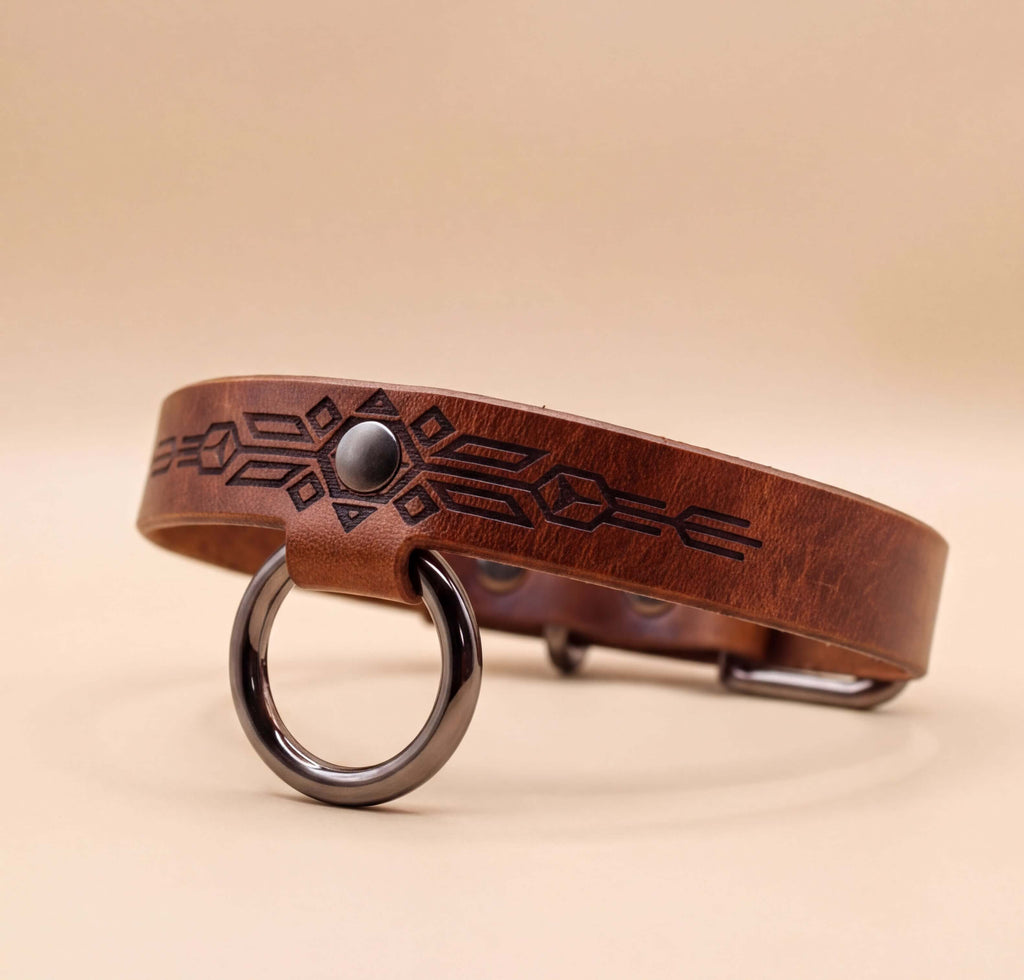 A brown leather dog collar with a metal ring and a decorative pattern on the leather.