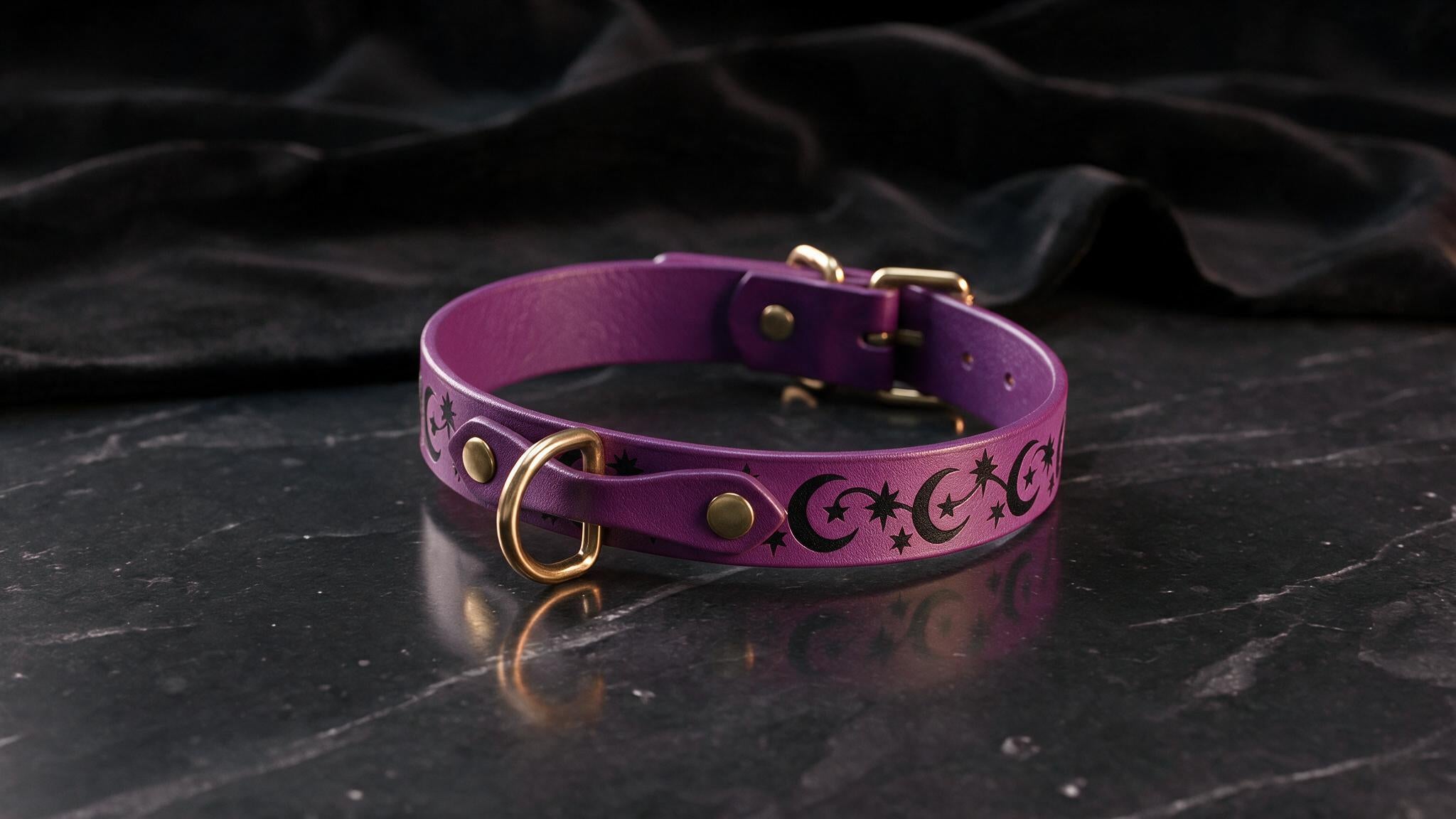 A purple leather collar with a star and crescent design on it, placed on a black marble surface.