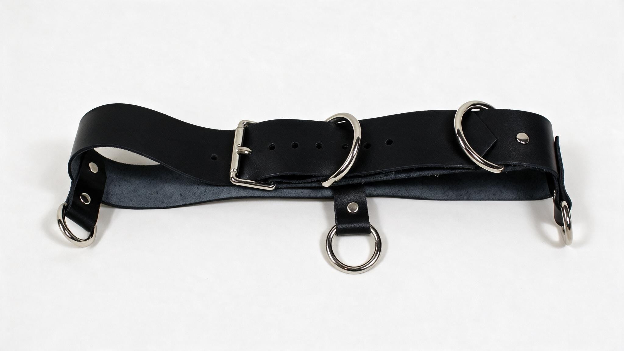 A black leather belt with metal rings and buckles, including a buckle and two rings, is shown in the image.