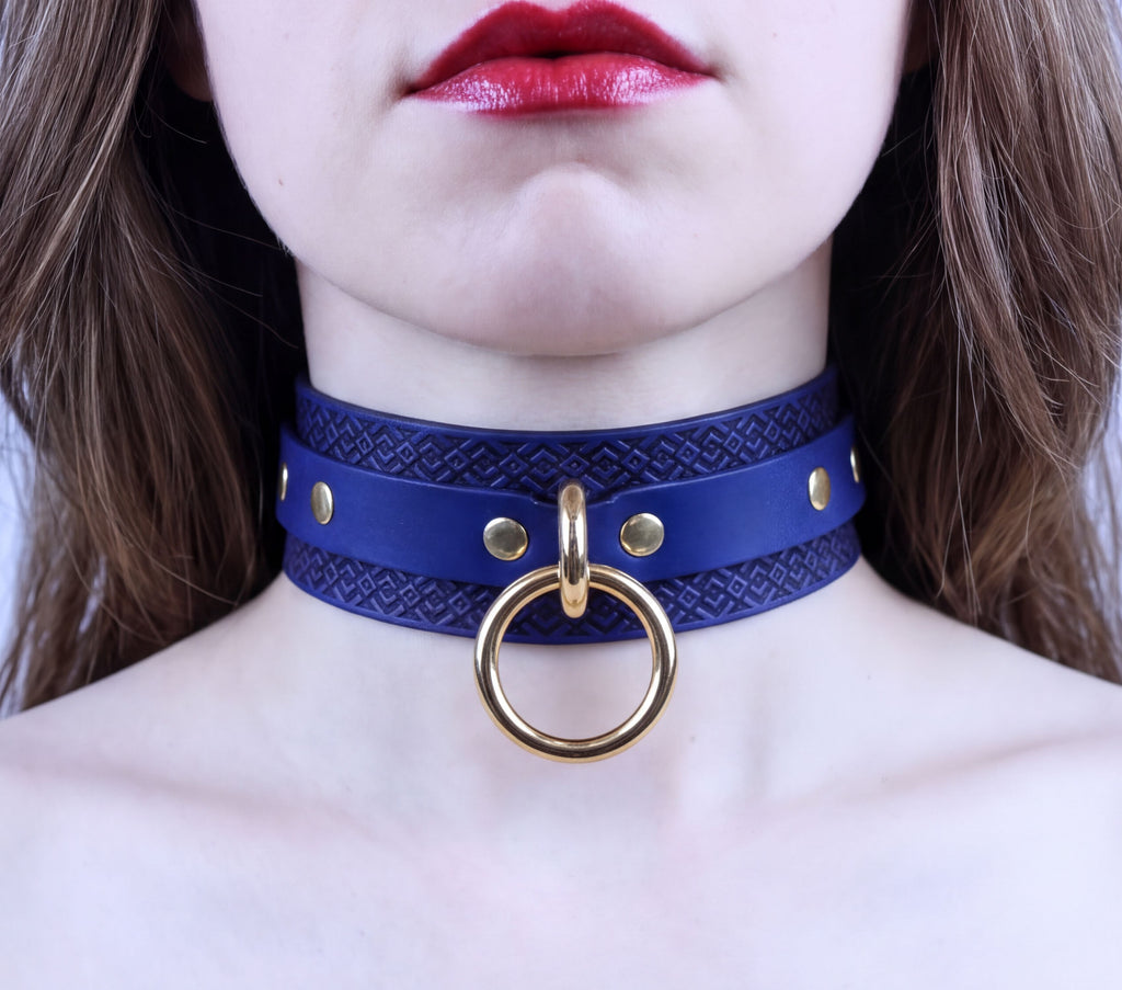 A close-up of a woman's neck and chest area, featuring a blue choker necklace with a gold ring and studs.