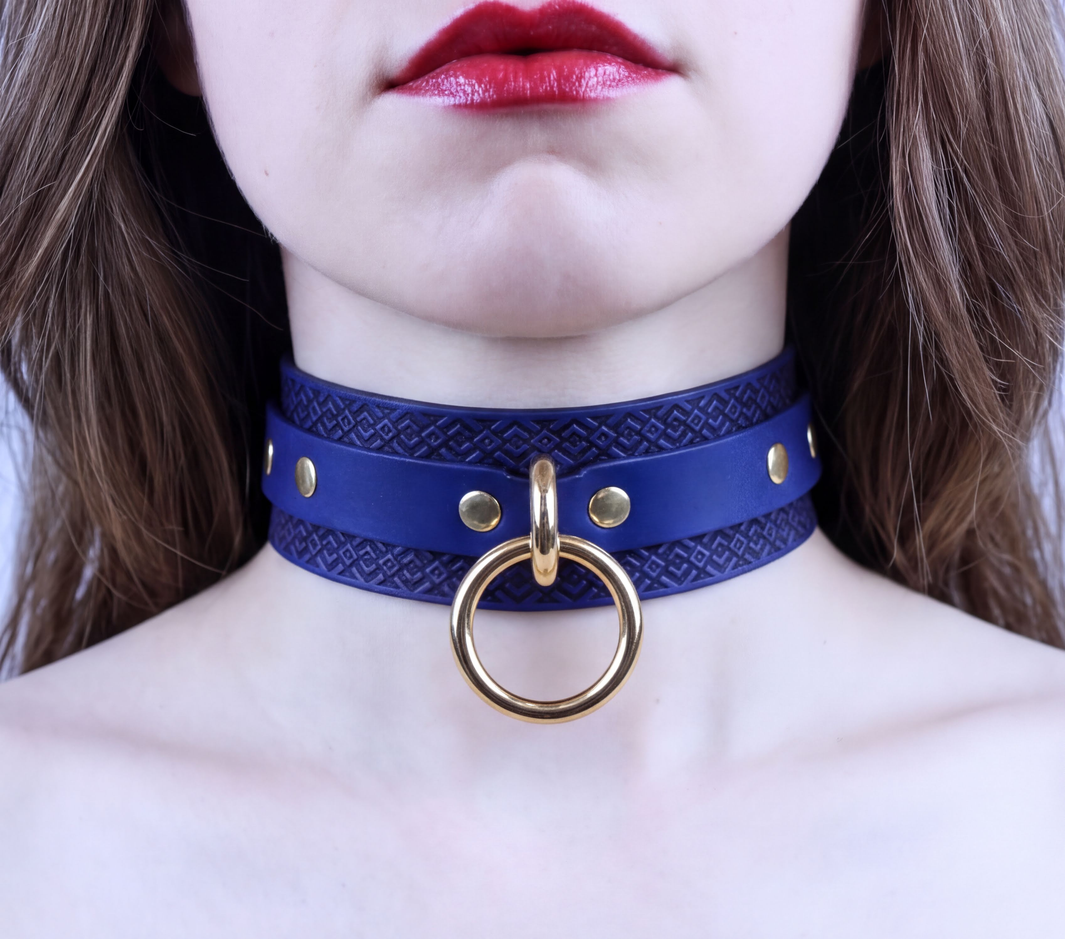 A close-up of a woman's neck and chest area, featuring a blue choker necklace with a gold ring and studs.