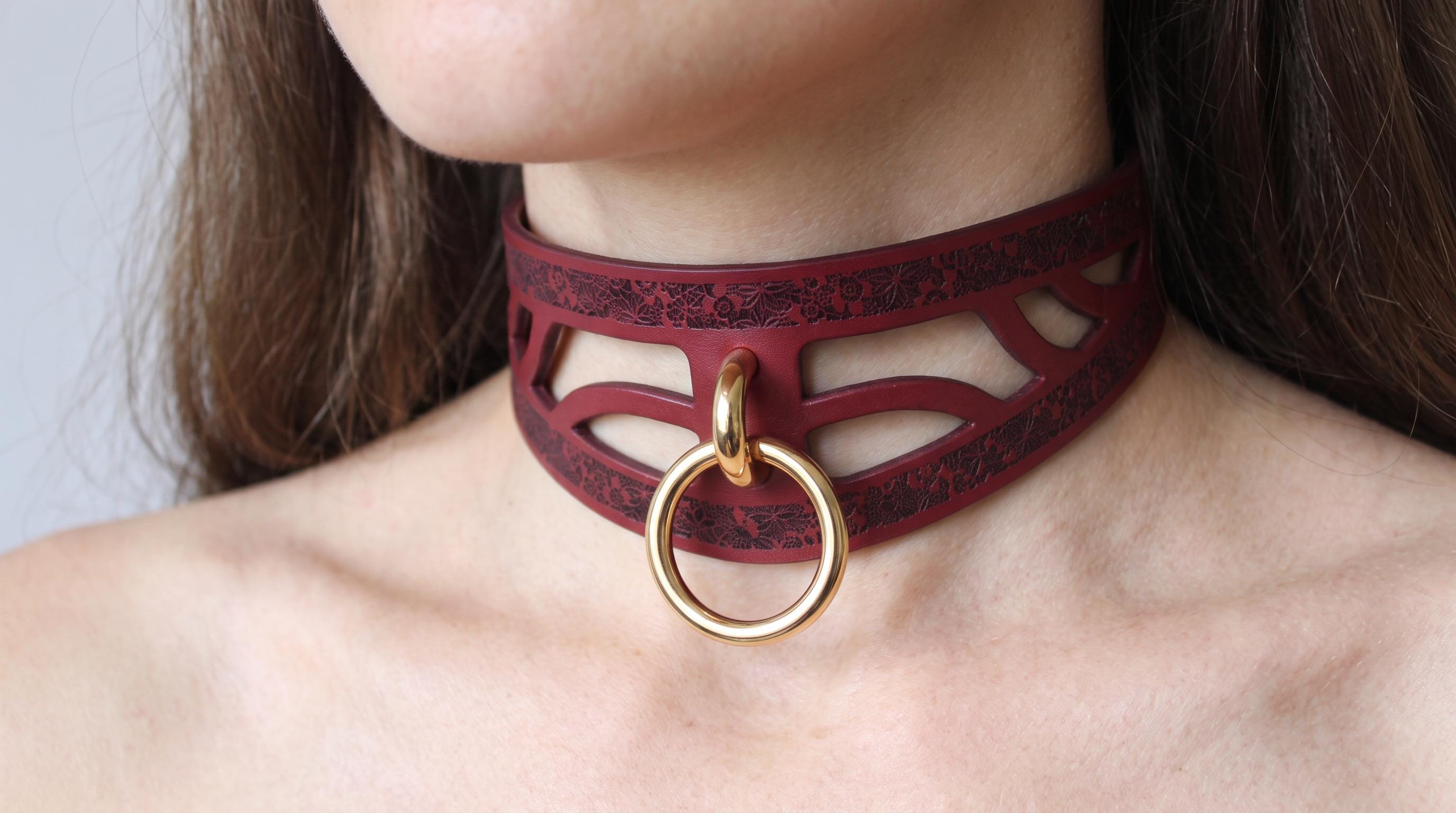 A close-up of a woman's neck wearing a burgundy choker necklace with a gold ring.