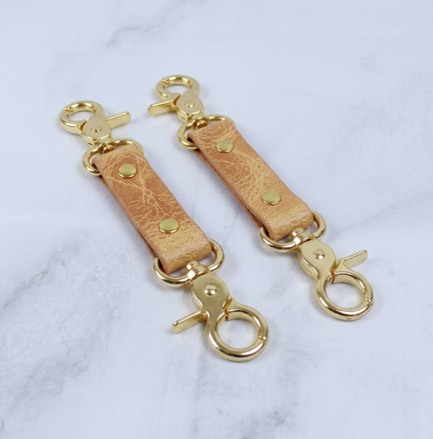 a pair of gold-colored leather straps with metal clasps, arranged on a white marble surface.