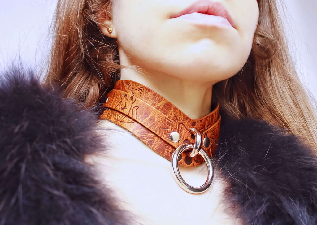 A close-up of a person's neck and chest area, featuring a leather choker necklace with a metal ring and a fur collar.