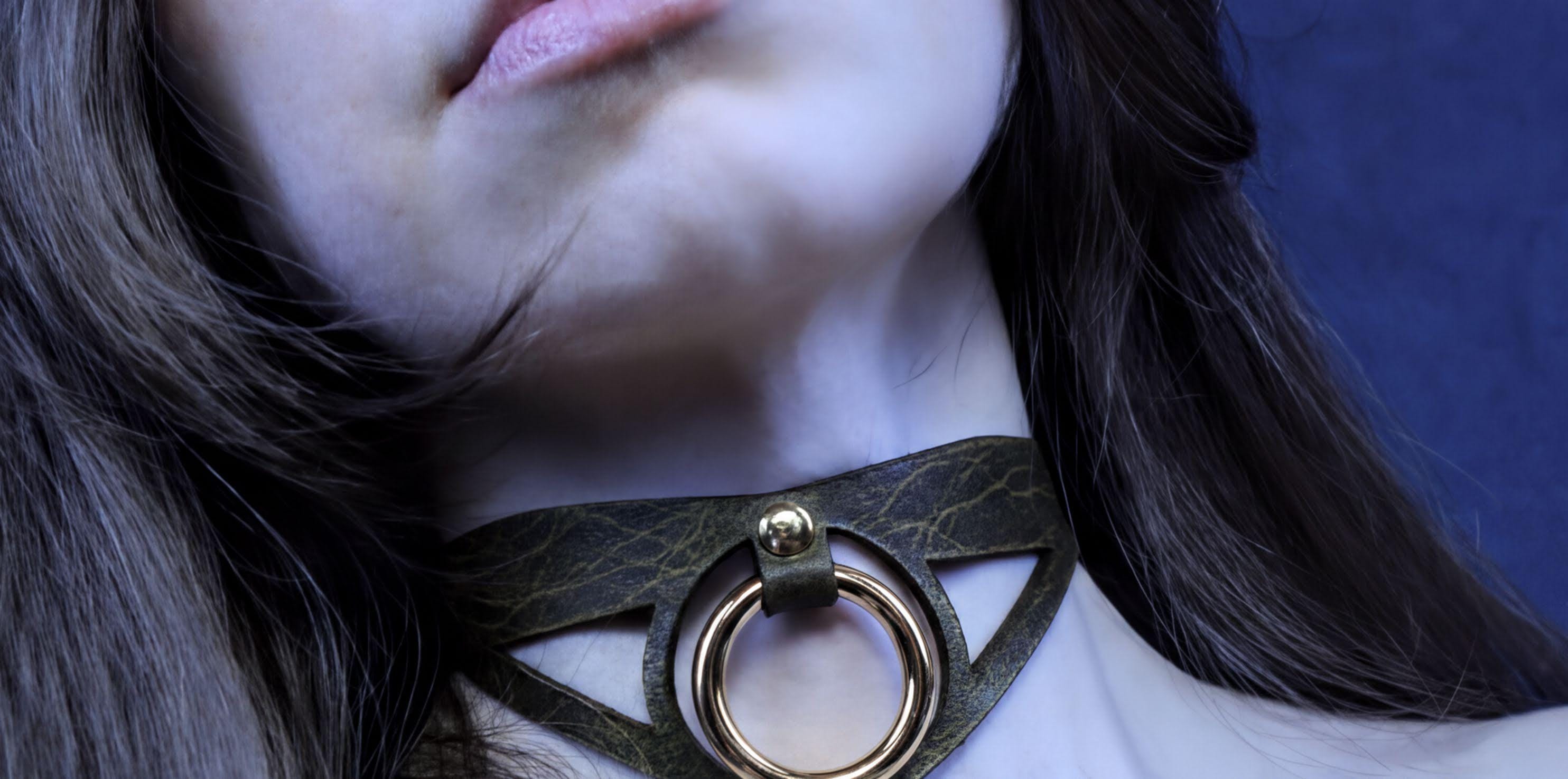 A close-up of a woman's neck and chin area, featuring a choker necklace with a circular metal ring.