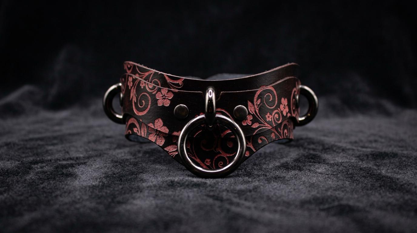 A dark leather choker necklace with a floral pattern and metal rings on the front.