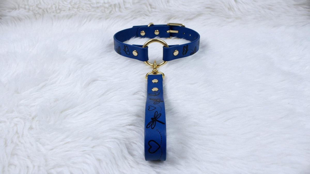 A blue collar with a gold buckle and handle is displayed on a white furry surface.