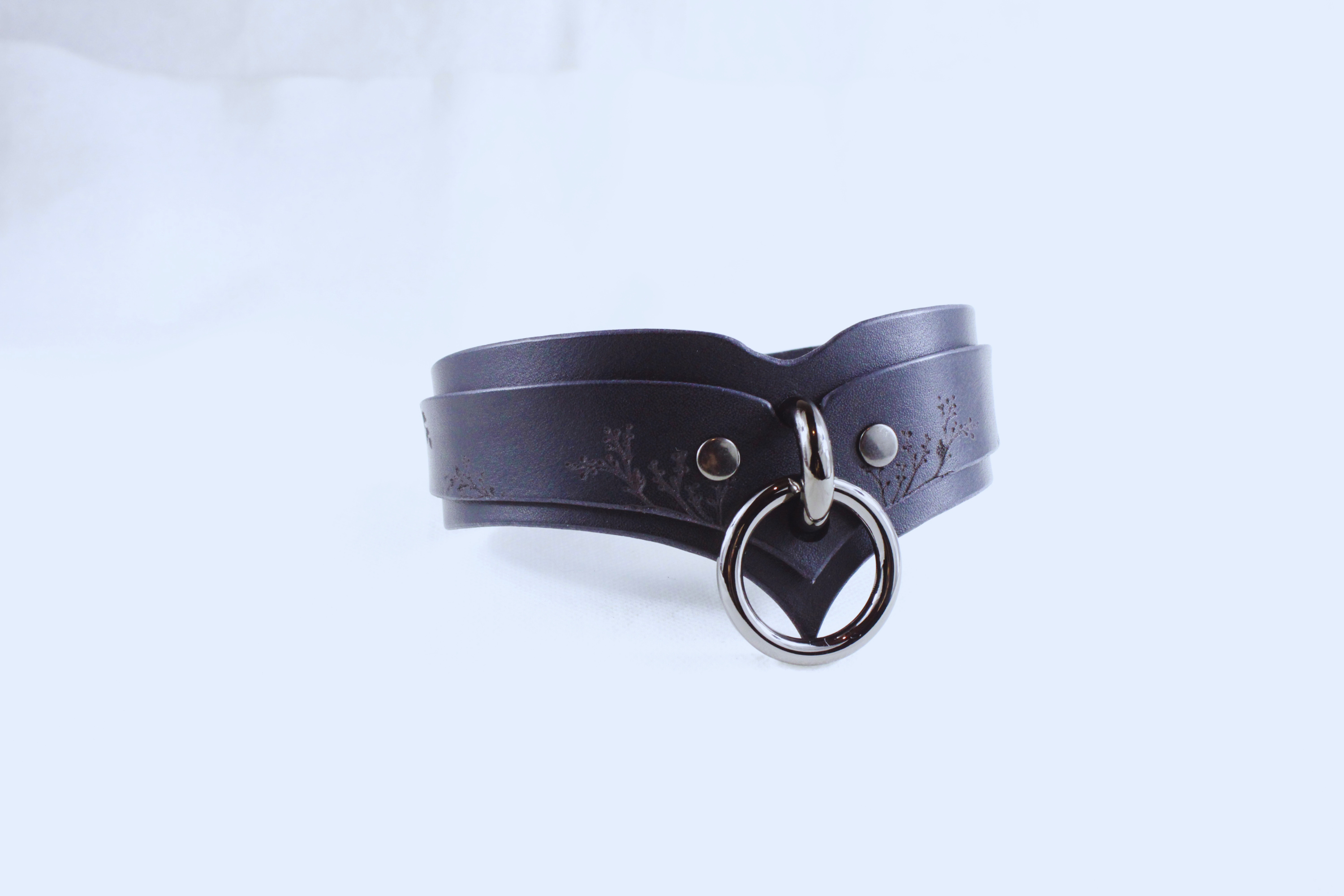 A black leather choker necklace with a metal ring and a decorative element on the front.