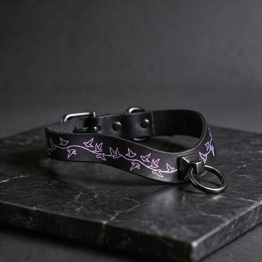 A black leather collar with a purple leaf design on it, resting on a dark surface.